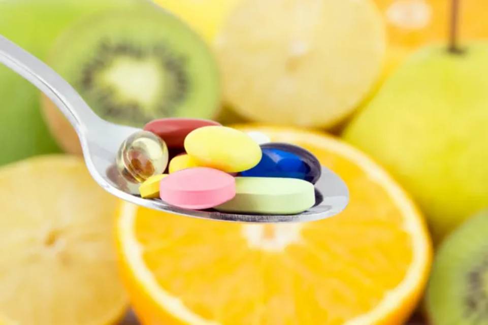 A spoon filled with pills and fruit on top of it.