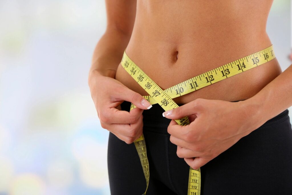 A woman is measuring her waist with a tape measure.